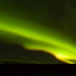 Iceland Aurora - a person standing on a hill looking at the sky
