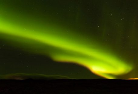 Iceland Aurora - a person standing on a hill looking at the sky