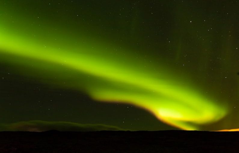 Iceland Aurora - a person standing on a hill looking at the sky