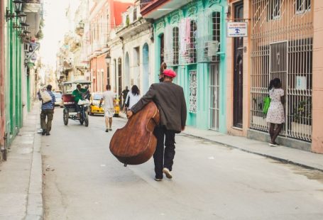 Old Havana - man carrying stringed instrument while walking the pavement during daytime