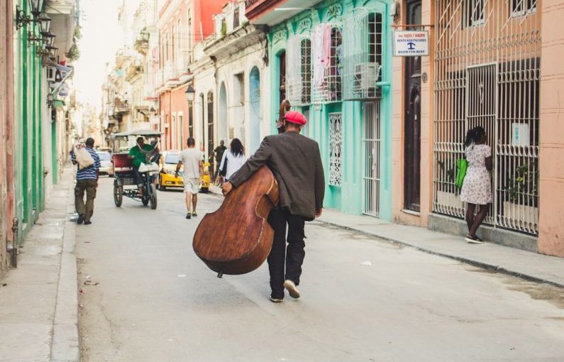 Old Havana - man carrying stringed instrument while walking the pavement during daytime